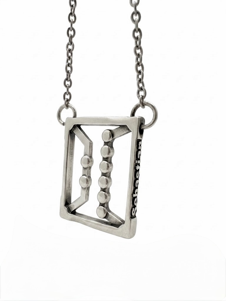 Finished cast sterling silver pendant on a chain, engraved with the name Sebastian, photographed on a white background